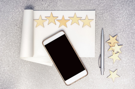 mobile phone, empty paper notebook, pen, five wooden stars in a row and group of stars at the side...