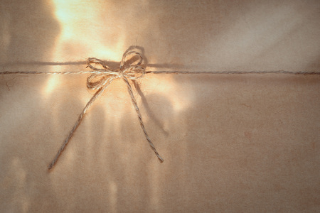 bow on a jute rope against a background of wrapping paper with sun lights spots on the paperの写真素材