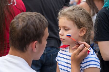 Moscow, Russia - June 23, 2018: man  drawing russian flag on the cheek of the young girl sport fan...