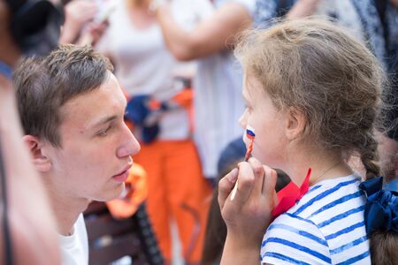 Moscow, Russia - June 23, 2018: man  drawing russian flag on the cheek of the young girl sport fan on the Nikolskaya street in Moscowのeditorial素材
