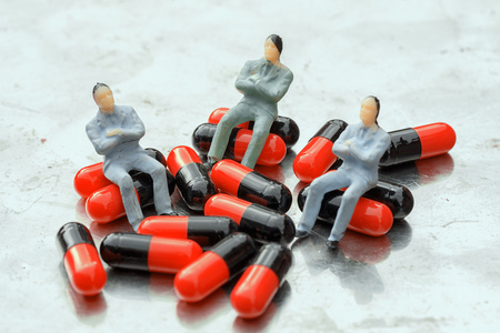 sit on pills. group of three miniature people toys men sitting on the heap red and black pills. health care concept.の写真素材
