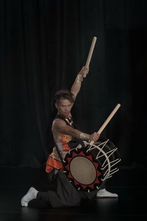 Full length portrait of a Japanese drummer Taiko on a dark stage.