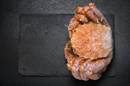 Icy hairy crab laying on the black table and slate board, top view with copy space.