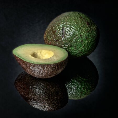 avocado on a black mirror surface with reflections isolated on black background.