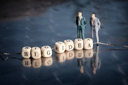 Miniature model of businessmen and wooden cubes with big idea inscription strung on a thread on reflective table.の写真素材