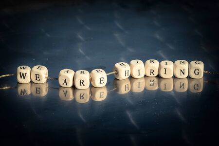 Wooden cubes with we are hiring inscription strung on a thread on reflective table. The recruitment business concept.の写真素材
