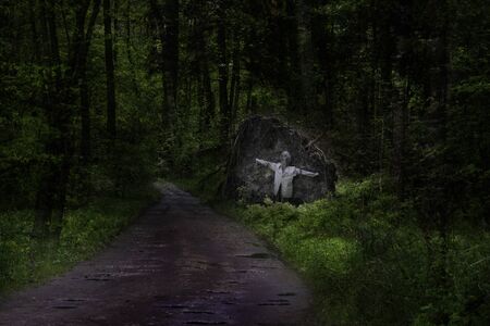 Horror. A figure in a gas mask and a shirt chained to a stone by the road in a dark forest.