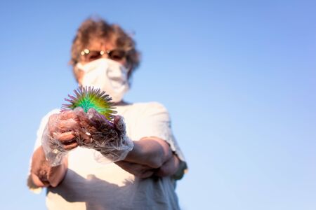 Protected by a mask and gloves, old woman holds a ball looks like coronavirus in her hands.の写真素材