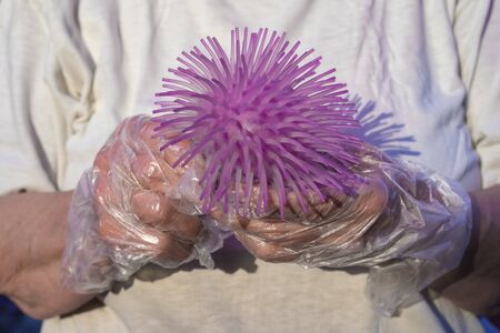 Protected by gloves, hands hold a ball looks like coronavirus close up.の写真素材
