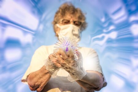 Old woman in mask and gloves holds virus ball in her hands.の写真素材