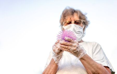 Old woman in mask and gloves holds ball looks like coronavirus in her hands.の写真素材