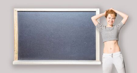 Happy young woman stands at the side of blackboard with copy space and straightens hairの写真素材