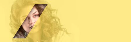 Beautiful girl with brown shadows and expressive eyebrows looks into the hole of yellow translucent colored paper. Fashion, beauty, make-up, cosmetics, beauty salon, style, personal care.の写真素材