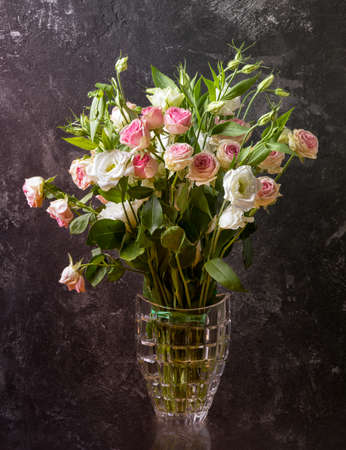 Eustoma and roses bouquet in vase on textured black wall background.の写真素材