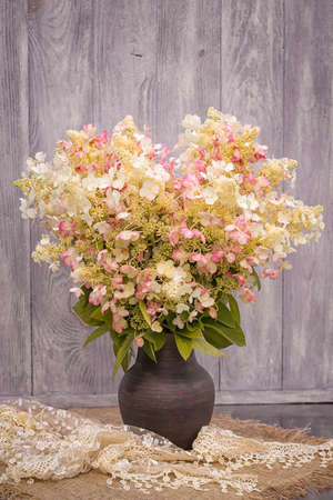 Bouquet of white with pink splashes of hydrangeas in a vase on the table against the background of a wooden wall.の写真素材
