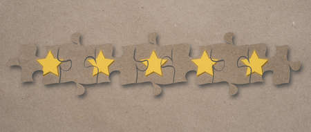 Five stars assembled on puzzle pieces against a craft paper background.の写真素材