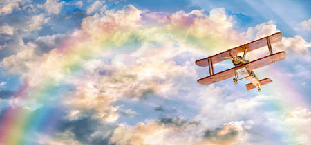 Toy plane is flying on a sunny day with a rainbow and clouds in the sky with copy space.の写真素材