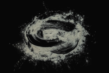 Black background sprinkled with flour, smeared flour, table for cooking, rolling dough. Preparing for baking, top view on a black background or table. Preparation of dough or dough.の写真素材