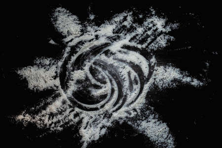 Black background sprinkled with flour sun shape, smeared flour, table for cooking, rolling dough. Preparing for baking, top view isolated on a black background or table.の写真素材
