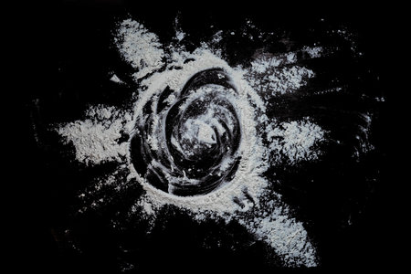 Black background sprinkled with flour sun shape, smeared flour, table for cooking, rolling dough. Preparing for baking, top view isolated on a black background or table.の写真素材