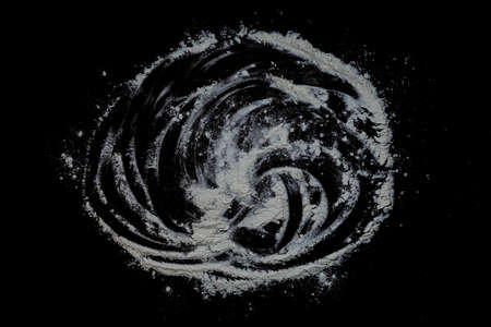 Black background sprinkled with flour, smeared flour, table for cooking, rolling dough. Preparing for baking, top view on a black background or table. Preparation of dough or dough.の写真素材