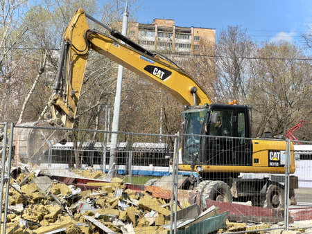 Moscow, Russia - April 28, 2022: Cat backhoe loader performs demolition work on a building on a city street.のeditorial素材