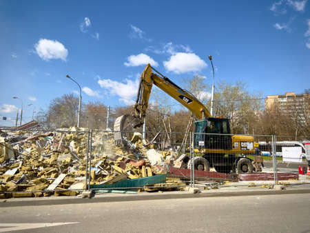 Moscow, Russia - April 28, 2022: Cat backhoe loader performs demolition work on a building on a city street.のeditorial素材