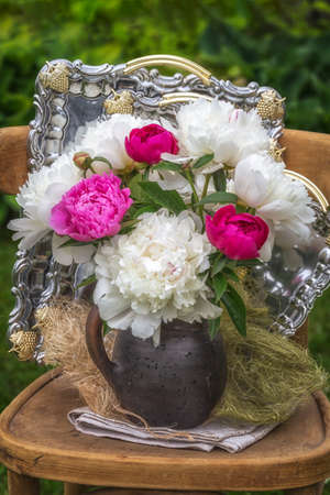 Bouquet of white and pink peonies in a jug on a chair and against the background of silver trays.の写真素材
