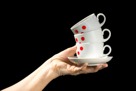 Coffee cups in red dots stack in hand isolated on black background.の写真素材