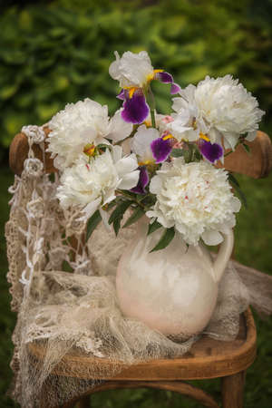 Bouquet of bearded irises and white peonies on a chair.の写真素材