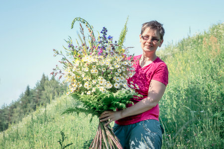 Woman holding a large bouquet of wild flowers with field daisies in her handsの写真素材