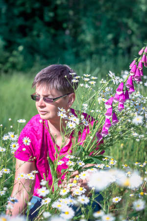 Woman collects a bouquet of wild flowers with daisies and foxgloveの写真素材