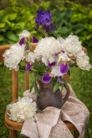 Bouquet of bearded irises and white peonies on a chair.の写真素材