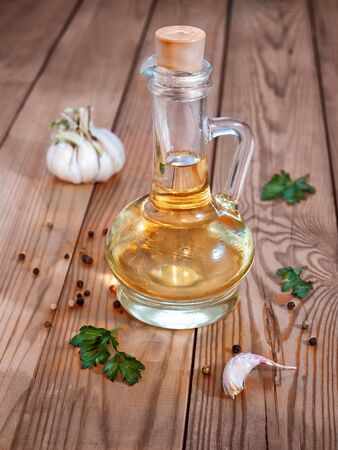 A glass decanter with vegetable oil on a wooden background surrounded by greenery, garlic and pepper is closed with a corkの写真素材