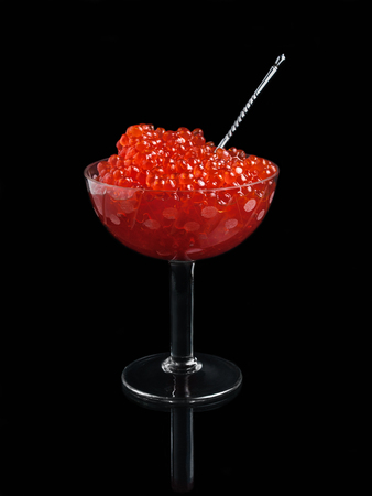 Sauteed red salted caviar in a glass vase with a spoon stands on a black background with reflectionの写真素材