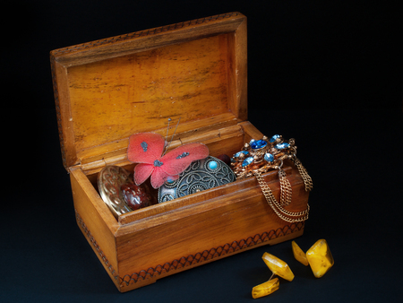 An open old wooden casket with old broken decorations inside and amber cuff links near the casket stand on a black backgroundの写真素材
