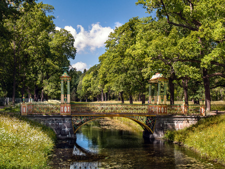 Stone bridge with gazebos and vases in Chinese style over the canal near the alley with lush green trees in the Alexander Park in Tsarskoye Seloの写真素材