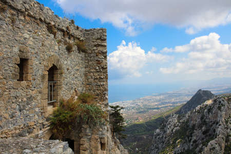Stone walls with arches of the castle of Saint Hilarion against a blue sky with clouds. The mountains of Cyprus and the view down to Kyrenia and the Mediterranean sea. Cyprus.の写真素材