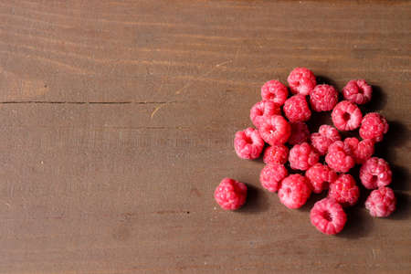 A handful of ripe, fresh, wild raspberries on a dark brown wooden Board.の写真素材