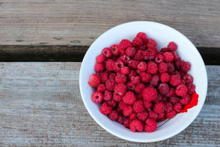 Top view of a white plate with fresh forest raspberries, standing on the right on a gray wooden bench. Eco-friendly, healthy food.の写真素材