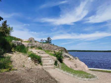 A stone staircase on the shore of the Vyborg Bay in the Monrepos Park of the city of Vyborg against the background of a blue sky with clouds.の写真素材
