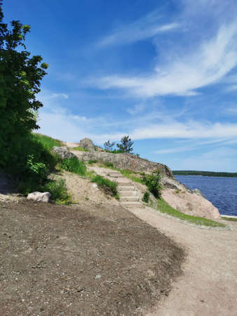 A stone staircase on the shore of the Vyborg Bay in the Monrepos Park of the city of Vyborg against the background of a blue sky with clouds.の写真素材