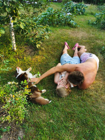 A young man and a woman are lying on the grass, a man is stroking a dog through a girl-a brown Welsh corgi cardigan.のeditorial素材