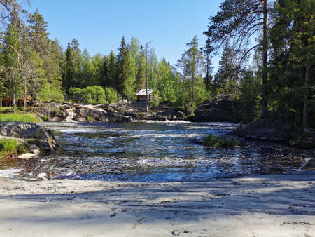 The picturesque waterfalls on the Tokhmayoki River, on the bank of which there is a wooden house,...