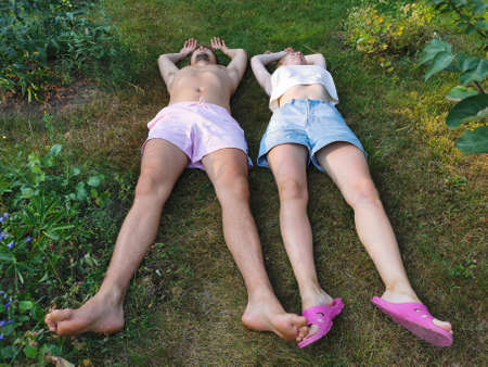 A young man in shorts and a woman in a top and shorts are lying on their backs and resting on the grass. Top view from the side of the legs.のeditorial素材