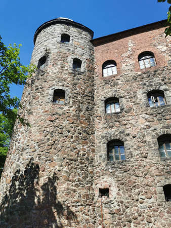 The outer stone wall and tower of the Vyborg castle in the city of Vyborg against the background of the blue sky and tree branches.のeditorial素材
