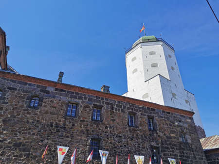 Against the blue sky, the stone wall of Vyborg Castle, flags and the white Tower of St. Olaf in the city of Vyborg.のeditorial素材