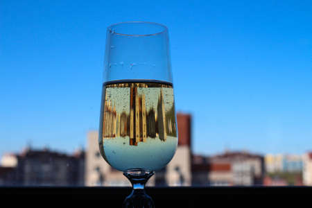 A glass of sparkling wine on the window, it reflects the houses and the sky.の写真素材