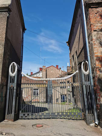 Forged black gates leading to a courtyard covered with cobblestones with low-rise old houses on a sunny summer day in Vyborg.の写真素材