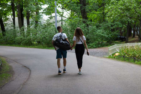 A girl and a young man walk hand in hand along the path of the Park on a summer day.